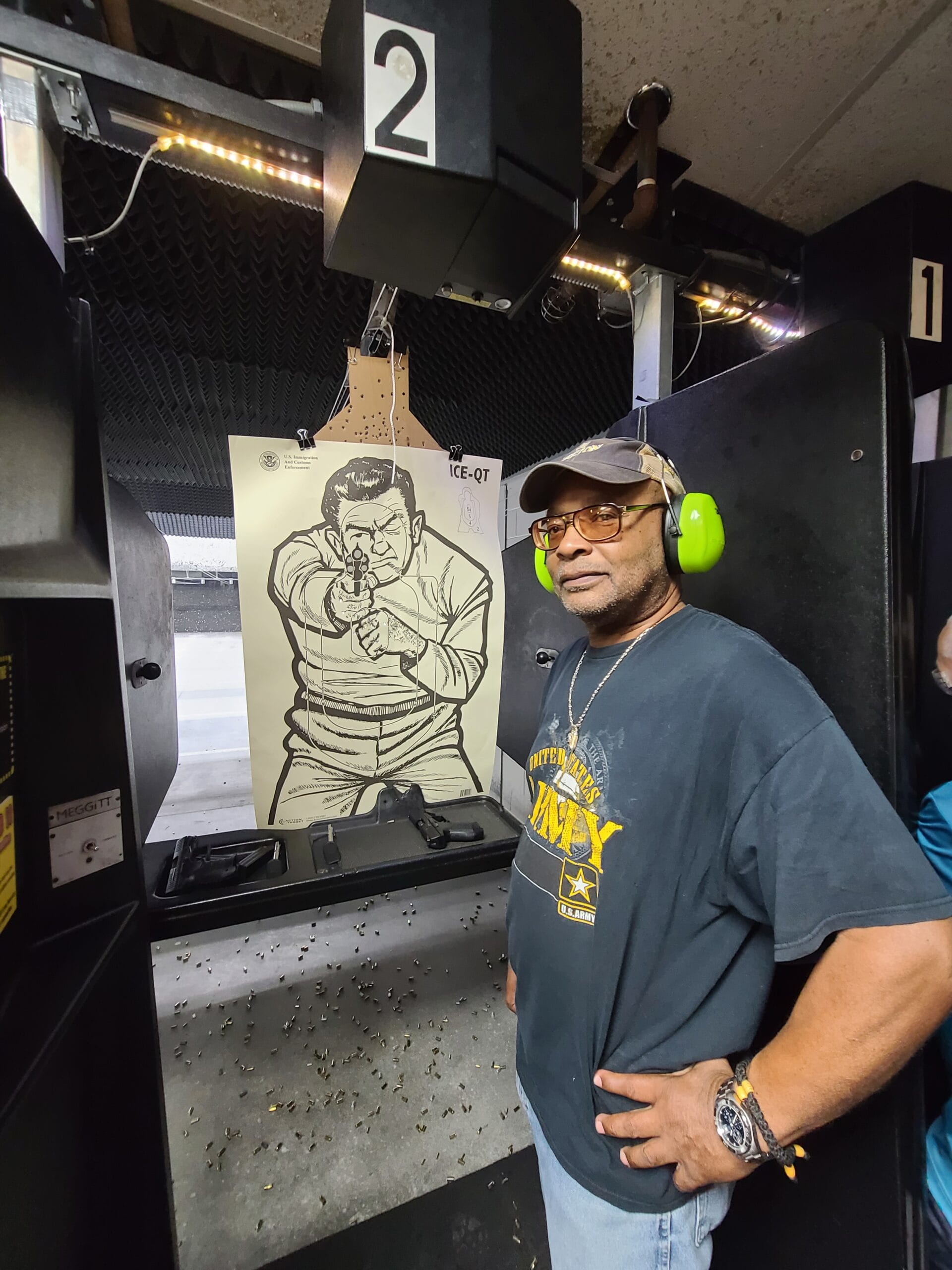 A student stands at the range bench where two pistols and their magazines are laid out, his target hanging in the lane behind him
