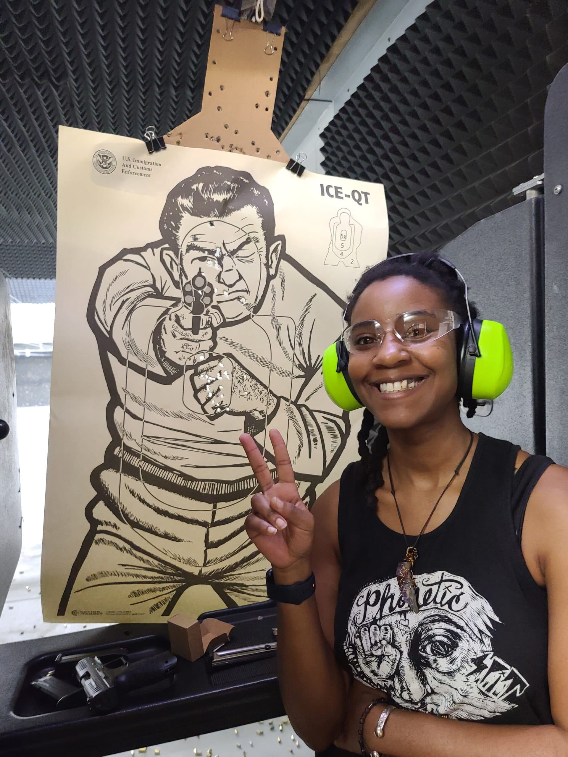 A student smiling beside the paper target she has just finished shooting, in eye protection and ear defenders