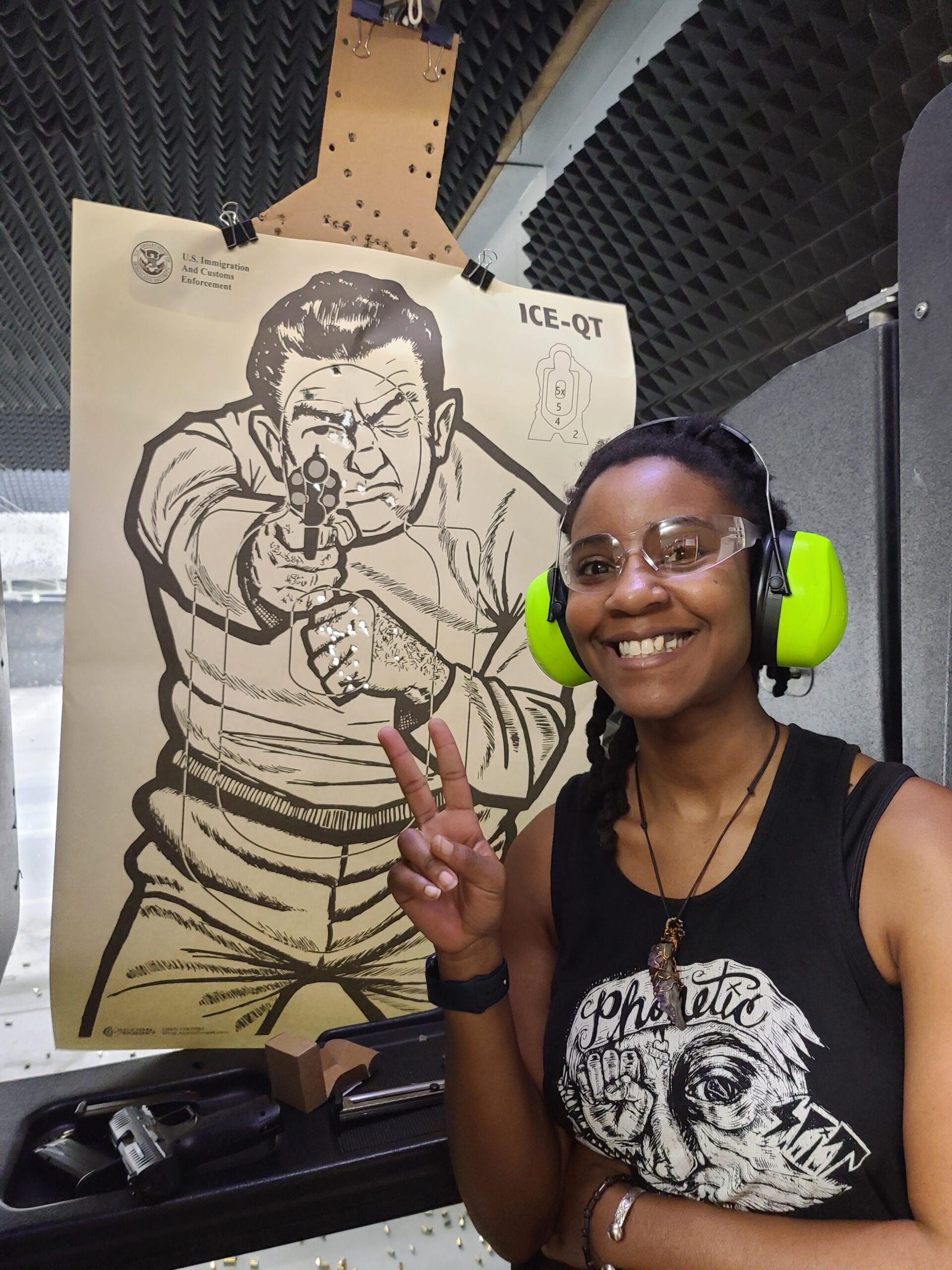 A student in eye and ear protection smiles beside her target at the end of a range session