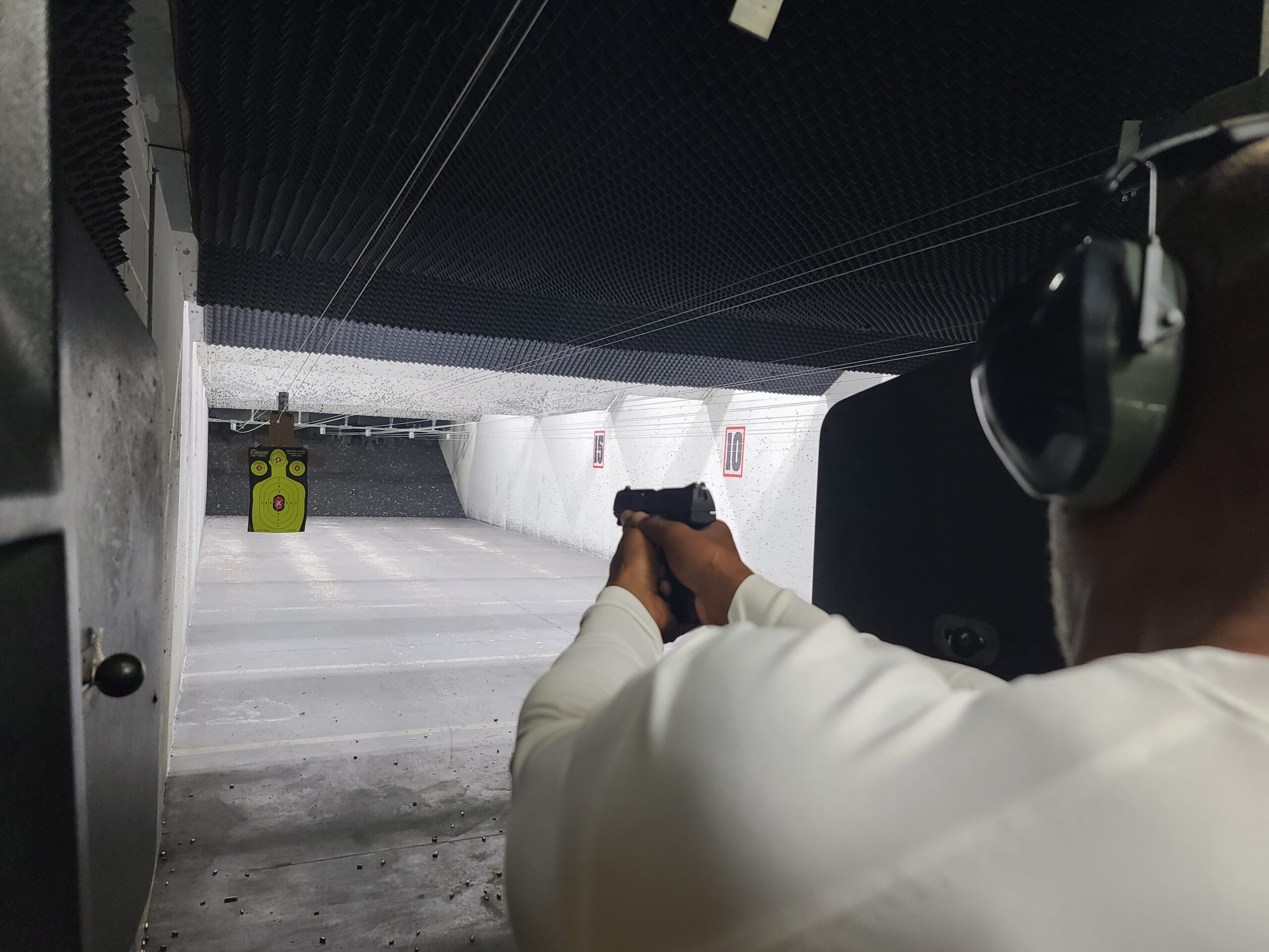 The view down an indoor range lane from behind a student taking aim at a paper target during a one-to-one session
