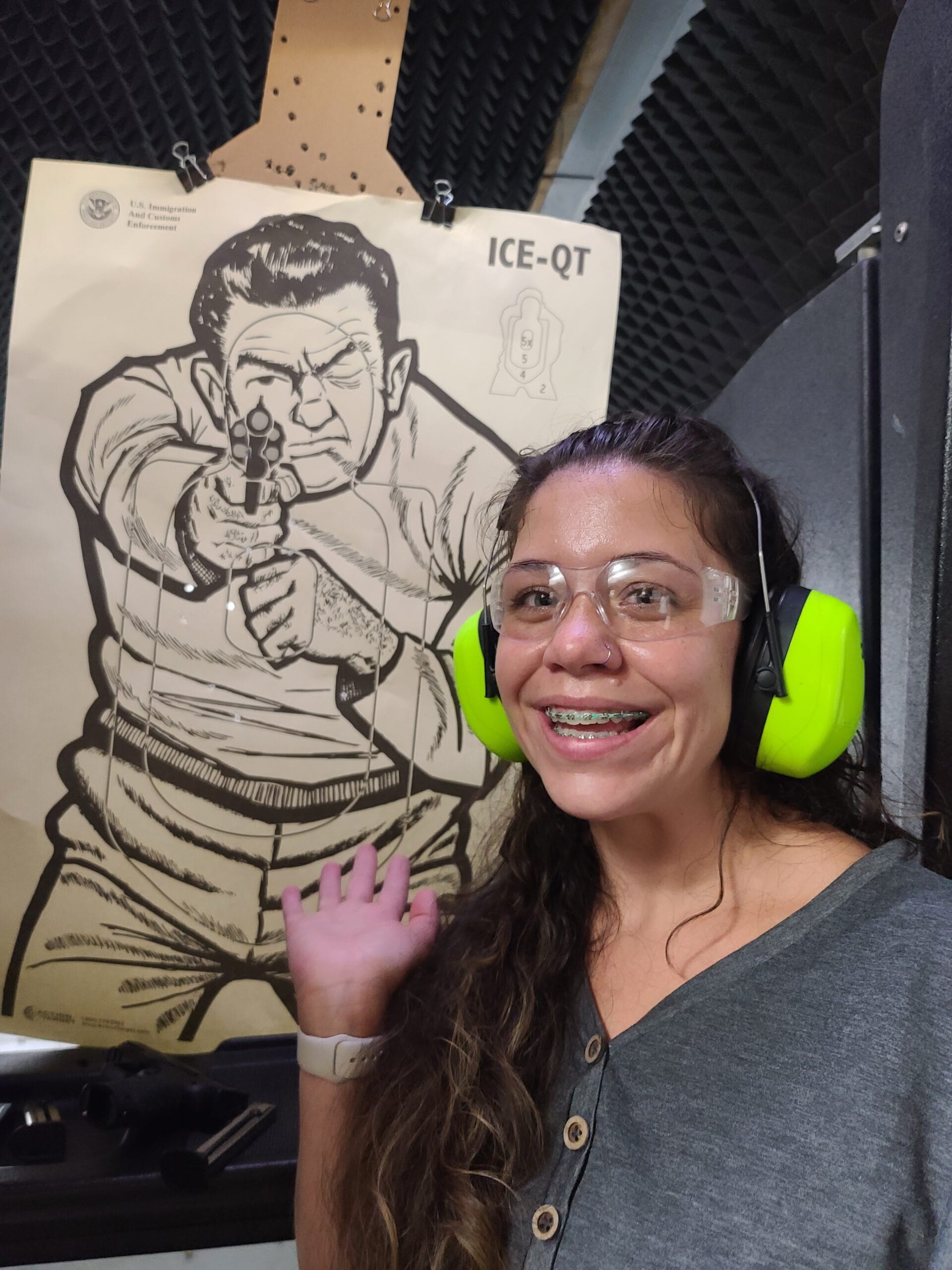 A student in bright green ear defenders waving beside her target at the end of a range session