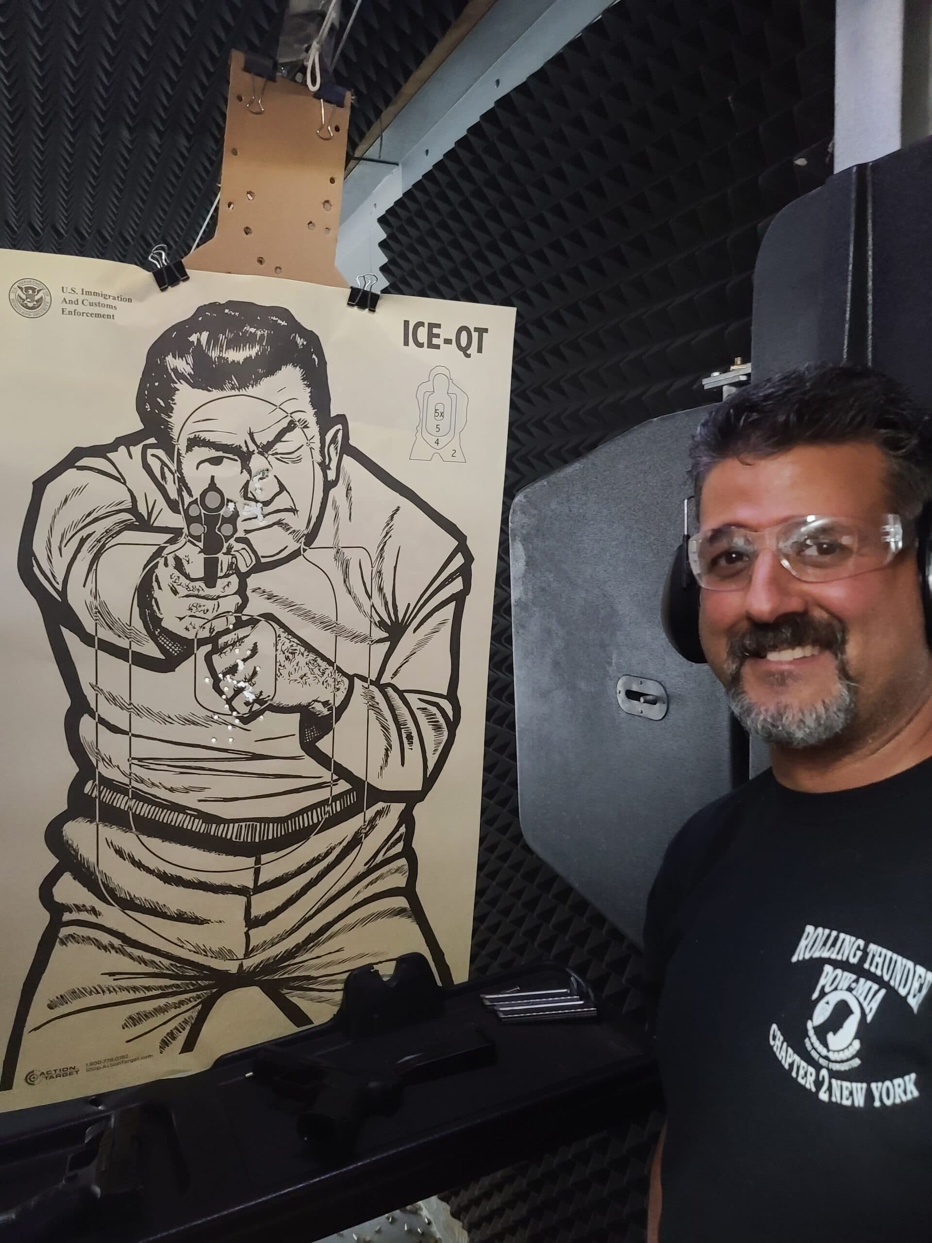 A student in safety glasses smiling beside his shot target at the end of a class