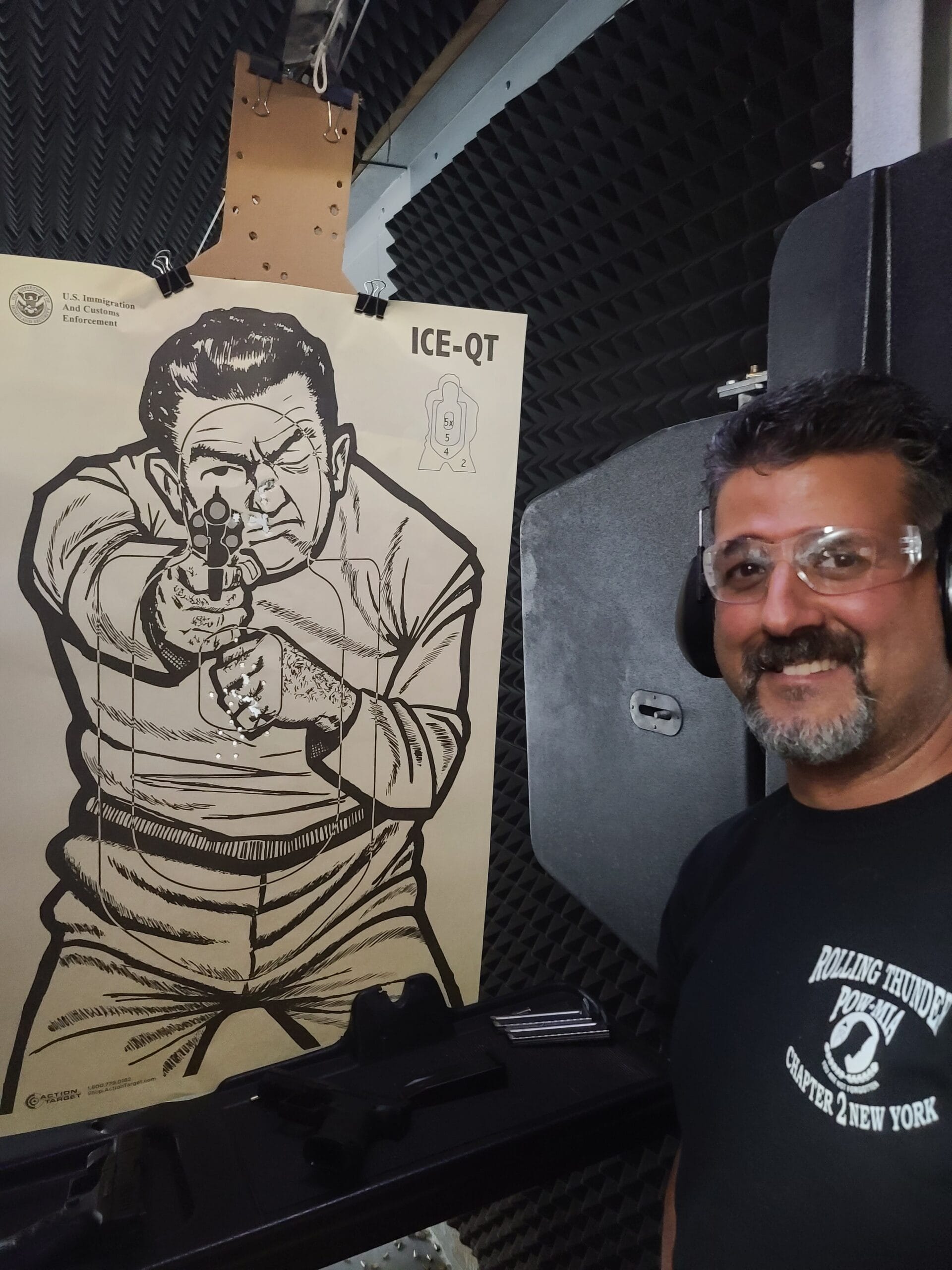 A student in safety glasses smiling beside his shot target at the end of a class