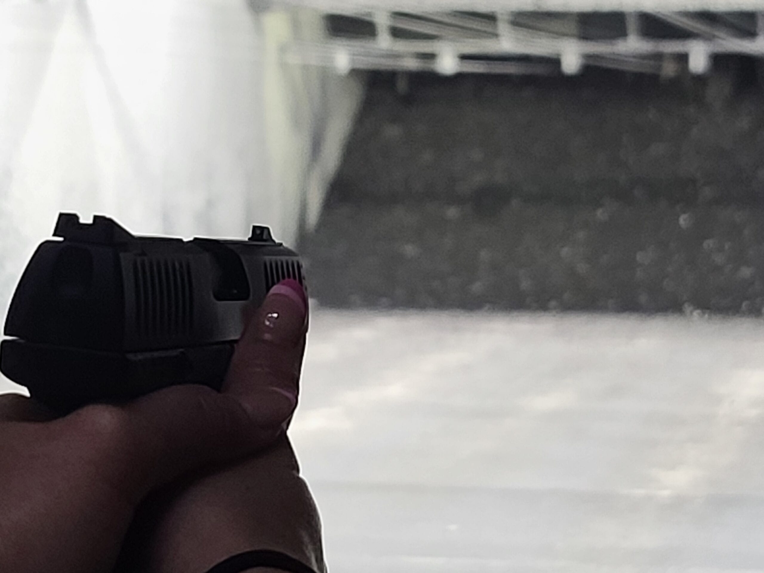 A close view of a shooter’s grip on a pistol with the sights aligned down a brightly lit range lane